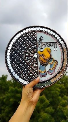 a hand holding up a decorative plate with an elephant on it's side and trees in the background