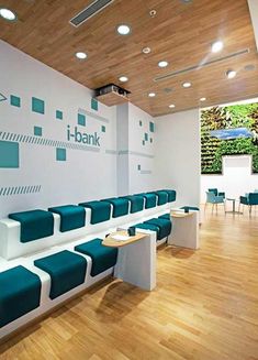 an empty waiting room with blue and white benches on the wall, in front of a plant covered wall