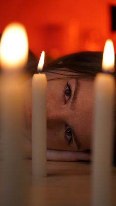 a woman laying on the floor in front of some candles with her eyes closed and one eye partially open