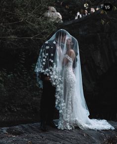 a bride and groom standing on a rock in the woods with their veil blowing in the wind