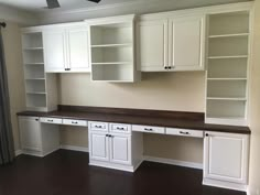 an empty room with white cabinets and dark wood flooring in the middle of it