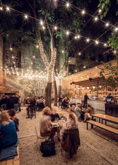 people are sitting at tables in an outdoor area with string lights strung over the trees