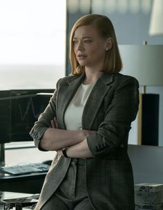 a woman standing in front of a computer desk with her arms crossed and looking off to the side