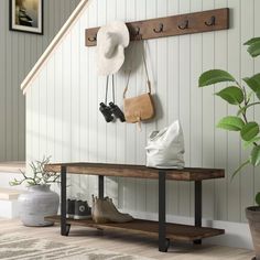 a wooden bench with hats and purses hanging on the wall next to a potted plant