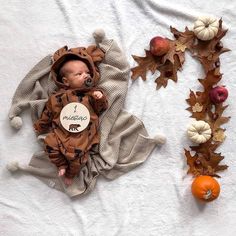 a baby laying on top of a white blanket next to pumpkins and other decorations