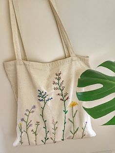 a white tote bag with flowers on it next to a green leafy plant