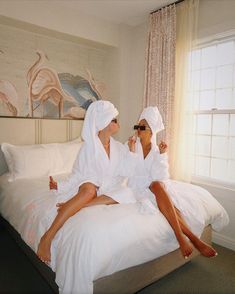 two women in white robes sitting on a bed