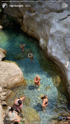 several people are swimming in the water near some rocks and boulders, while one person is taking a photo