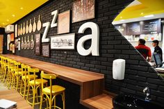 the interior of a restaurant with yellow stools and black brick walls, along with pictures on the wall