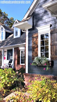 a gray house with white trim and shutters on the windows is surrounded by greenery