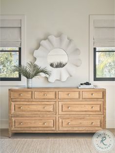 a room with a dresser, mirror and plants on the sideboard in front of two windows