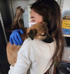 a woman holding a dog in her arms and wearing blue gloves on it's head