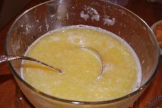 a glass bowl filled with liquid sitting on top of a wooden table next to a metal spoon