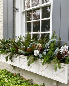 a window sill filled with pine cones, evergreen and other greenery in front of a brick building