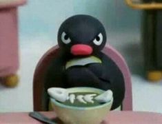 a toy penguin sitting at a table with a bowl of soup