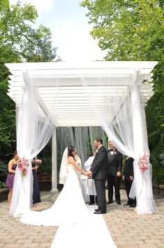 the bride and groom are getting married in front of an outdoor gazebo with white drapes