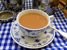 a cup of tea sits on a blue and white checkered tablecloth with spoons