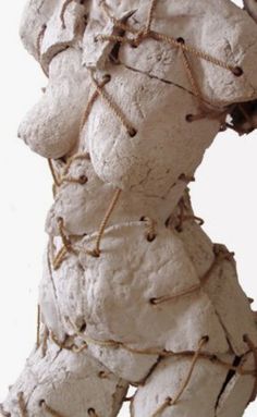 a white sculpture with brown string wrapped around it's neck and torso, against a white background