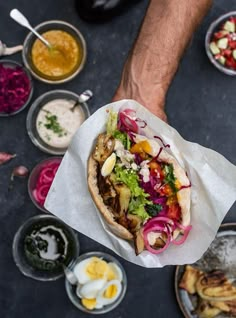 a person holding a taco in their hand with other food on the table behind them