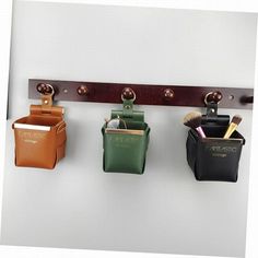 three leather pouches hanging on a wall with two metal hooks and one has a brush in it