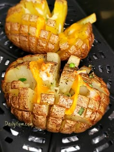 two baked potatoes with cheese and onions on a black grill grate, ready to be cooked