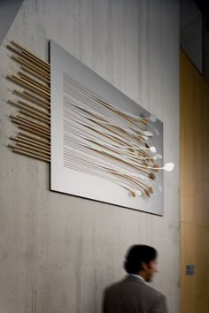 a man walking past a wall with a large art piece hanging on it's side