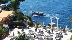 an aerial view of a boat in the water and people sitting at tables near it