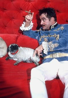 a man sitting on top of a red couch next to a small pug dog