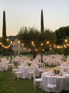 tables and chairs are set up for an outdoor wedding reception in the grass with string lights strung over them