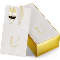 a white box with gold foil and a fork in it, sitting next to a paper bag