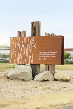 a wooden sign sitting on the side of a dirt road next to rocks and grass