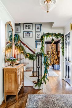 a christmas garland is hanging on the bannister in this entryway decorated with greenery and gold ornaments