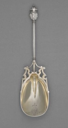 a silver spoon hanging from the side of a metal hook on a gray wall with an ornate design