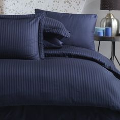 a bed with blue sheets and pillows on top of it next to a night stand