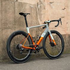 an orange and grey bike leaning against a stone wall with no wheels on the front