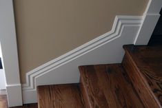 an open door on the side of a stair case next to a wooden floor with white trim