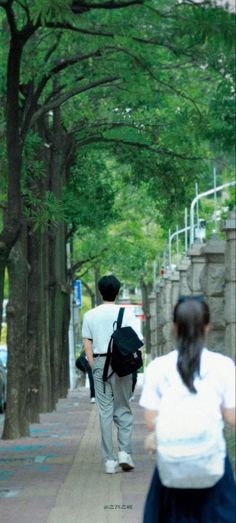 two people are walking down the sidewalk with backpacks on their back and one is carrying a book bag