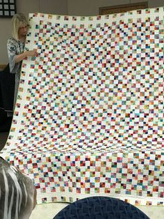 a woman is holding up a quilt made with squares and strips in the center, while another person looks on