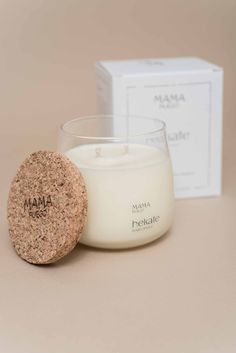 a white candle sitting next to a box on top of a brown table with a cork coaster in front of it