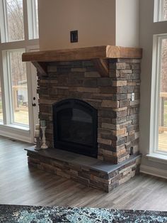 a living room with a stone fireplace and large windows in the back wall, along with hardwood flooring