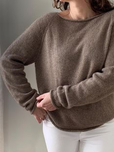 a woman standing in front of a window wearing a brown sweater and white pants with her hands on her hips