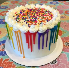 a cake with white frosting and rainbow sprinkles on the top is sitting on a colorful tablecloth