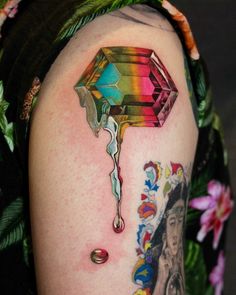 a woman's arm with tattoos on it and a colorful diamond dripping from the top