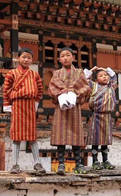 three young boys standing on top of a wooden platform in front of an old building