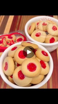 two white bowls filled with cookies covered in red icing on top of a wooden table