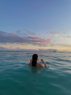 a woman sitting in the water with her hand up to her face while looking at the sky