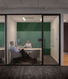 two people sitting at desks in an office with green and white striped wallpaper