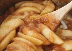 apples are being cooked in the pot with a wooden spoon and some brown sauce on top