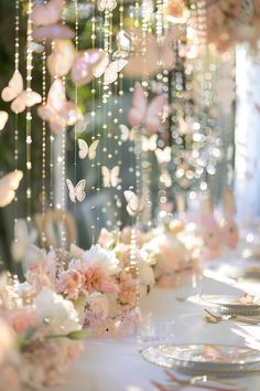 the table is set with pink flowers and butterflies hanging from it's ceilings