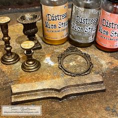 three bottles and two candles sit on top of an old book that has been turned into a candle holder